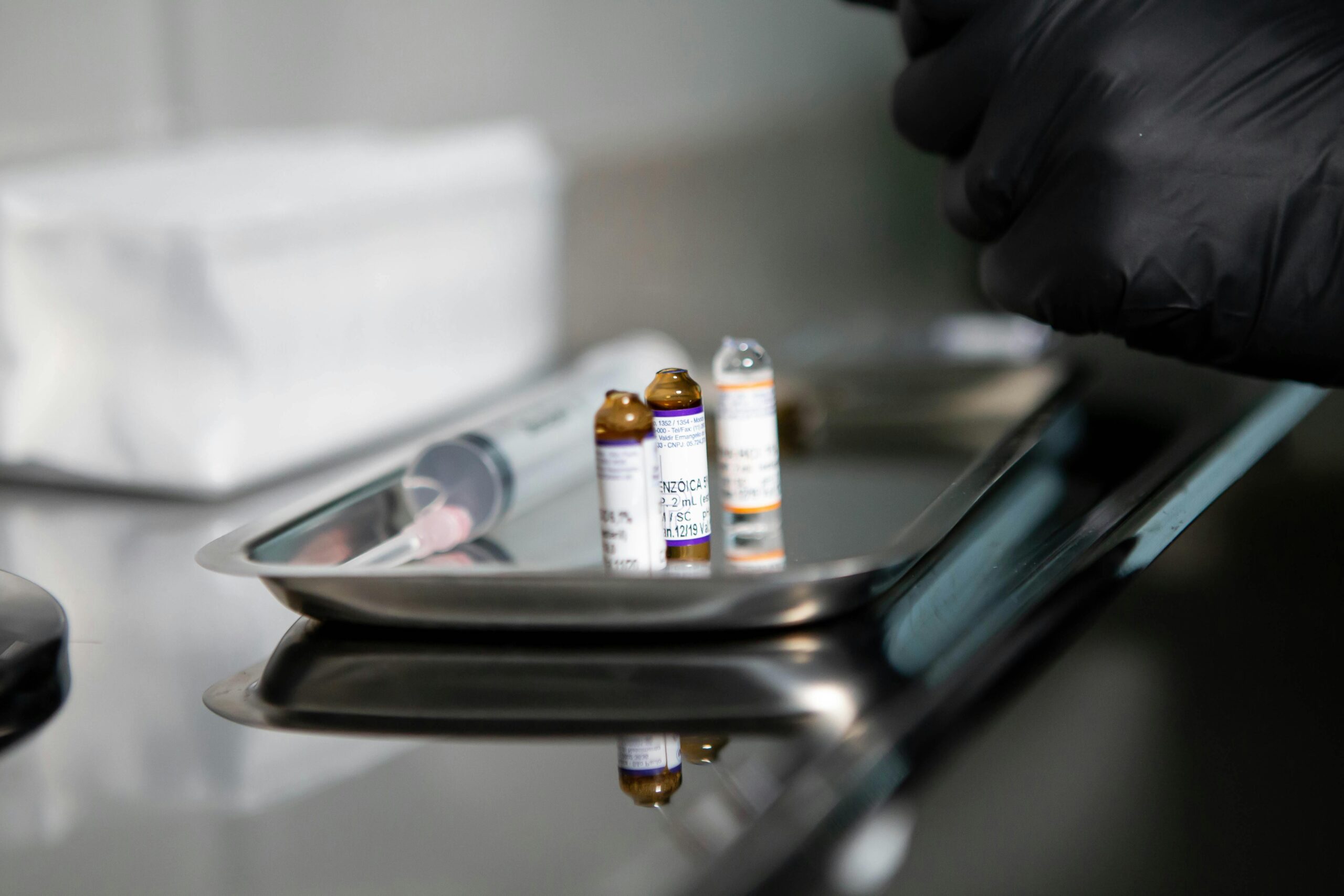 Close-up of medical vials and syringe on stainless tray in clinical setting.