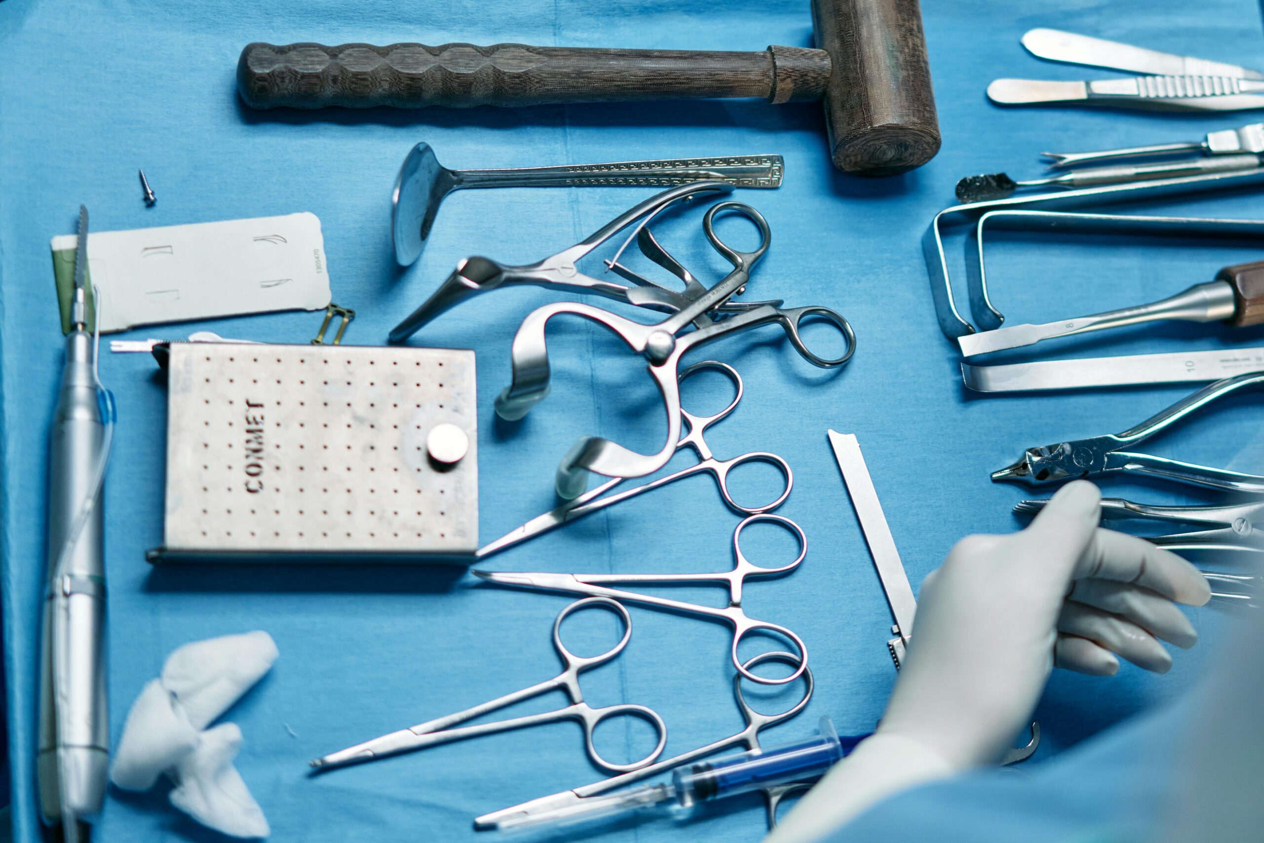 Close-up of various surgical instruments on a blue sterile sheet in a medical setting.